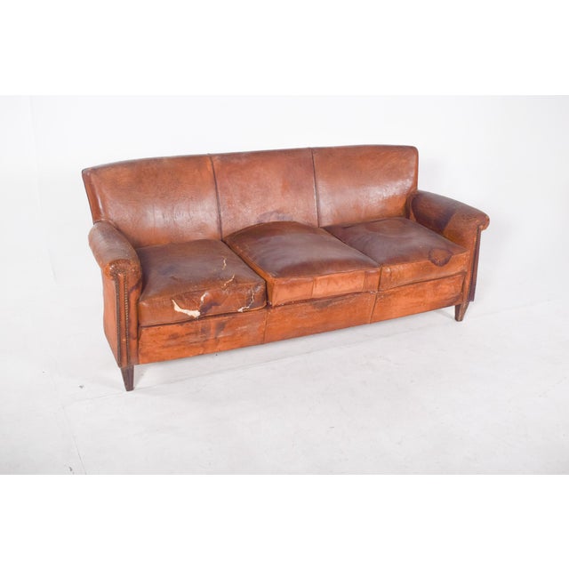 Three-seater sofa, brown leather. The leather shows clear signs of wear, with visible tears, stains and dry areas,...