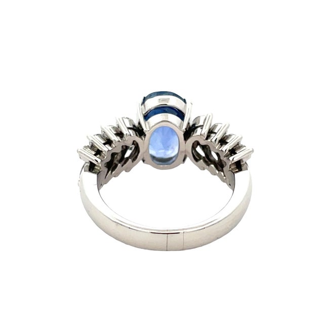 Elegant platinum ring centered with a striking 3.40 carat oval blue sapphire, beautifully accented by marquise-cut...