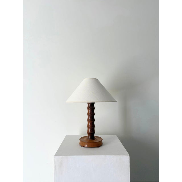 A hand turned wooden table lamp with a simple yet decorative stem, supported on a circular plinth base with squashed bun...