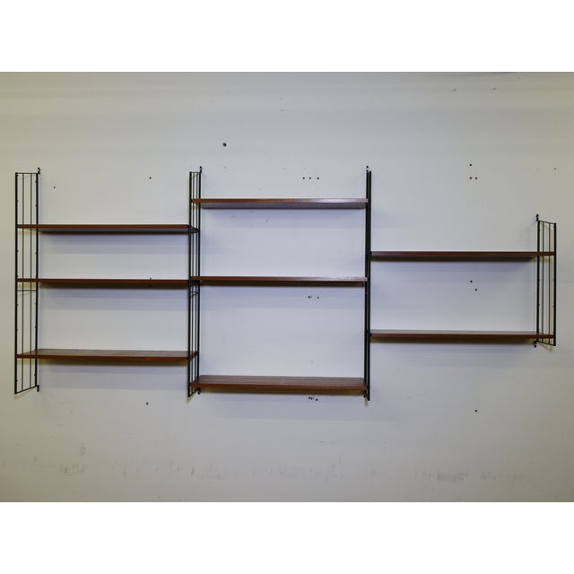 Modular String shelving unit in teak, 1960s. This wall-mounted unit consists of six black metal ladders and nine teak...
