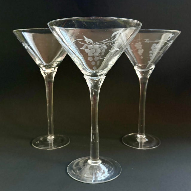Elegant set of three vintage clear glass martini glasses featuring a delicate etched grape and vine motif. The wide,...
