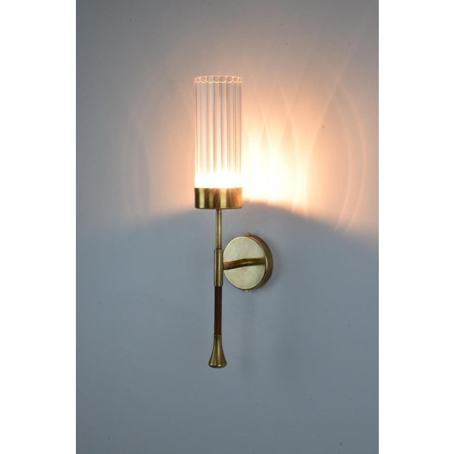 A timeless wall light built in a solid brass structure highlighted by a leather-sheathed stem and a cylinder-textured...