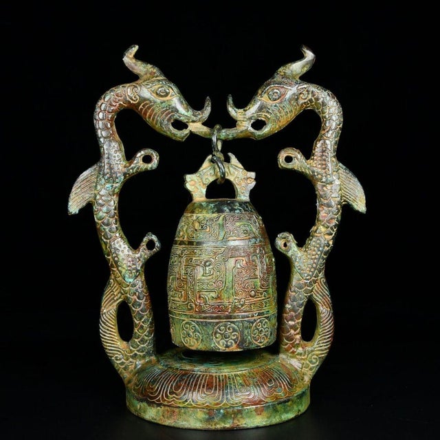 A striking Chinese bronze sculpture featuring a central bell suspended within an ornate frame. The frame is formed by two...