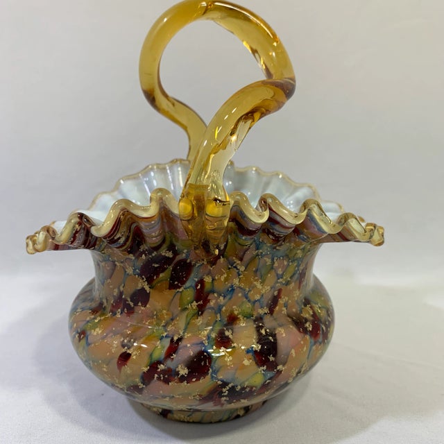 The art glass ruffled basket with amber handle showcases baby pink and blue reflecting light as its designed purpose. A...