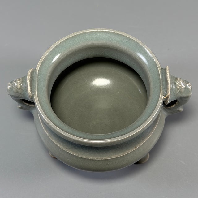 This Chinese Longquan celadon‑glazed porcelain incense burner is fitted with two exquisitely‑carved dragon‑form side...