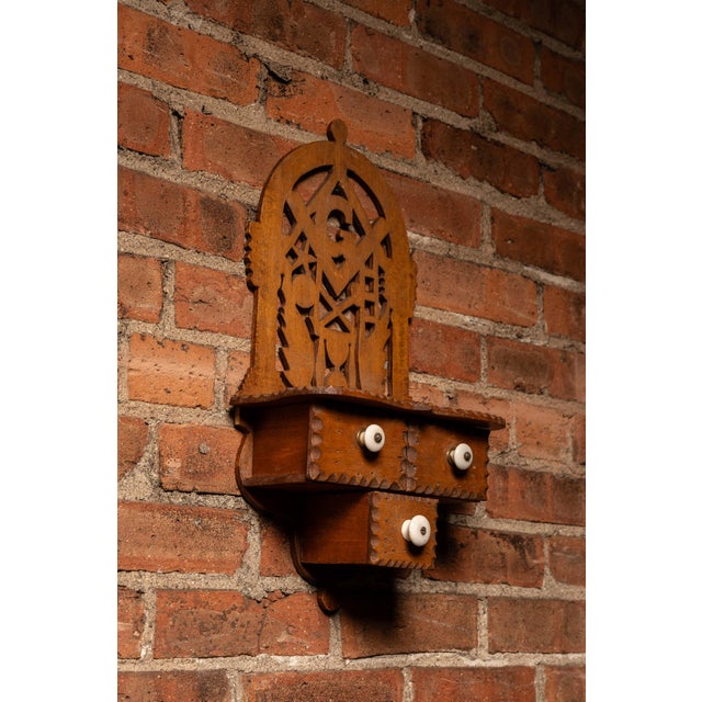 Hand-cut wooden wall cabinet featuring an elaborate openwork crest centered around Masonic iconography, including the...