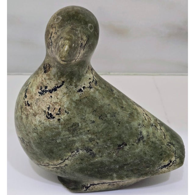 Signed in Inuit syllabics on the underside, this mid-century Inuit soapstone bird sculpture has a softly stylized bird...
