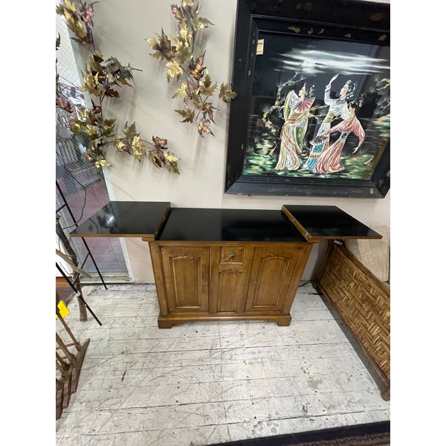 Warm-toned wood cabinet featuring paneled doors, carved details, and dual drop-leaf extensions that create a generous...