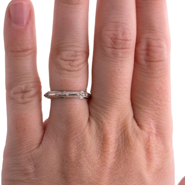 A 14k white gold wedding ring with a detailed design. The band features intricate engravings and a milgrain edge. The ring...