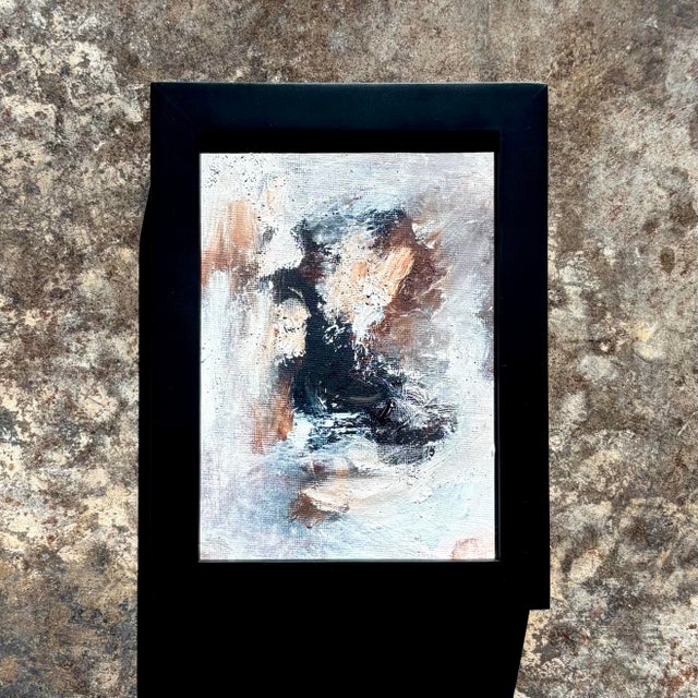 A softly textured abstract in layered dark blues, white, and warm brown tones, this painting evokes light moving across...