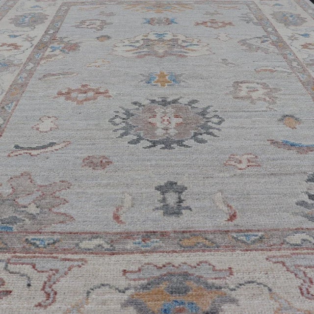 This piece gives a modern vibrancy to the classic floral Oushak design. With a light grey background, the field showcases...