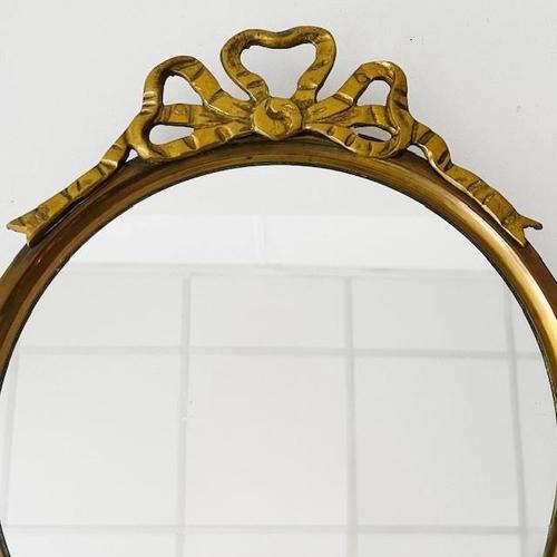 Vintage baroque round brass bow mirror in Hollywood Regency style from the 1960s. This mirror is a true beauty in gold. It...