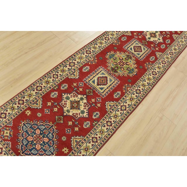 A tribal Caucasian Kazak runner hand-knotted with fine wool on a cotton foundation. This rug features a row of geometric...
