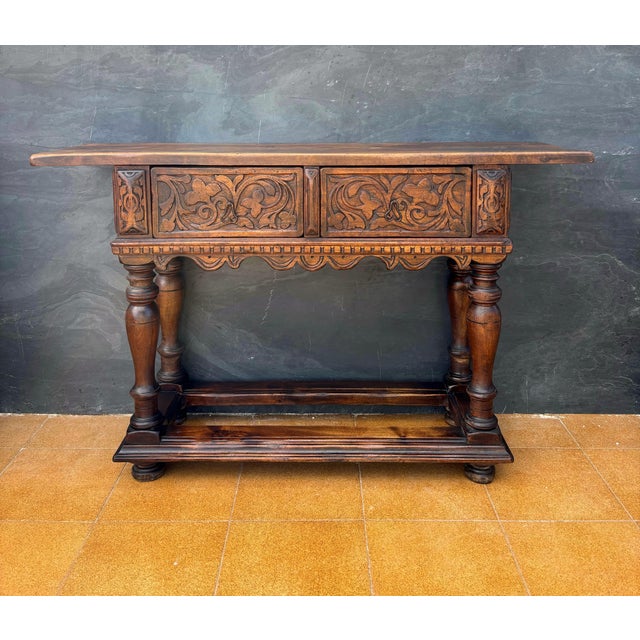 Spanish Renaissance Revival console crafted in solid oak, featuring two deeply carved drawers and a structural lower...
