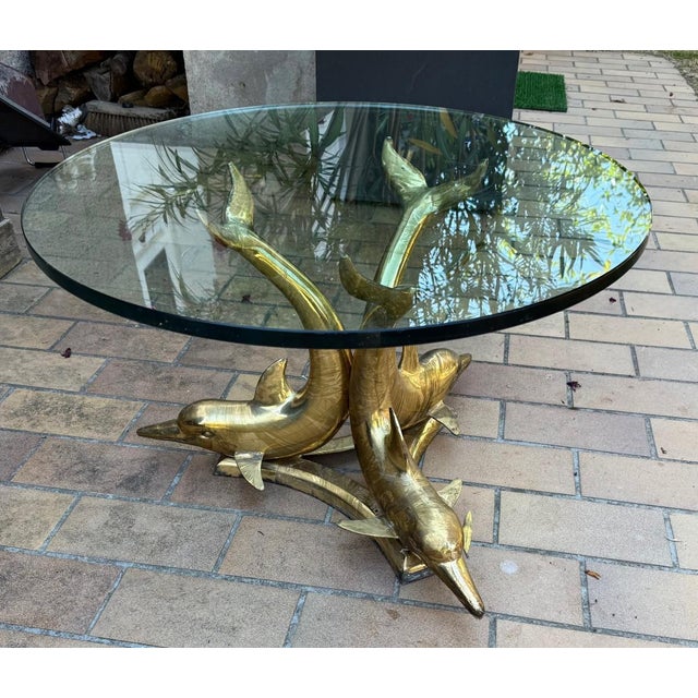 "Three dolphins coffee table" coffee table 20 mm thick glass top supported by three brass dolphins on a triangular support...