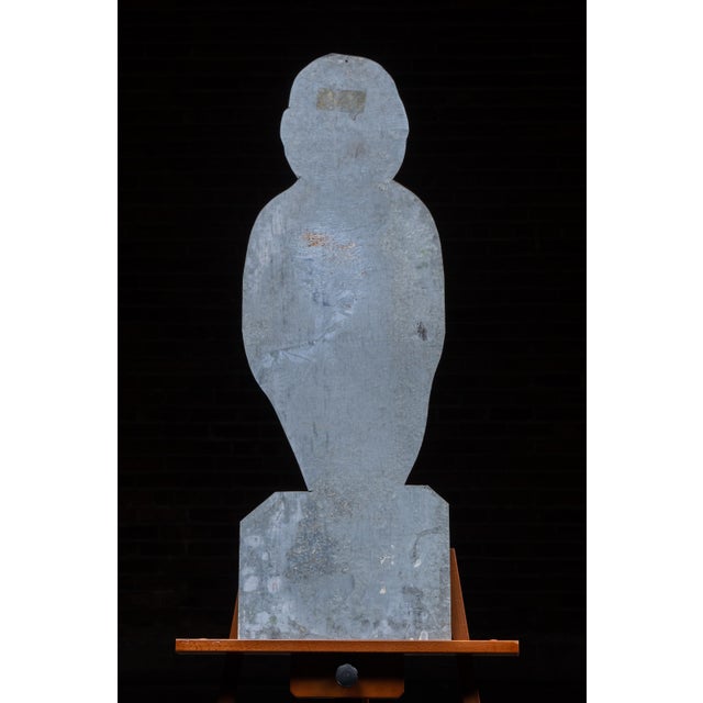 Die-cut tin advertising display in the form of a smiling, stylized gentleman dressed in a green suit with bowtie, hands...