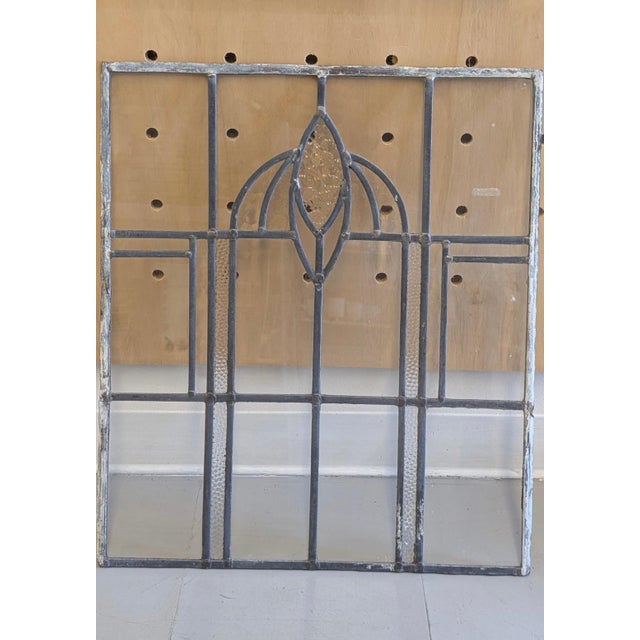 This likely antique leaded glass window panel features a symmetrical geometric design with a central stylized floral motif...