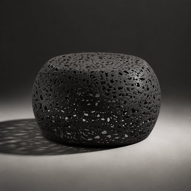 Black fiber openwork coffee table with a sculptural rounded form and intricate cutout pattern across the entire body. The...