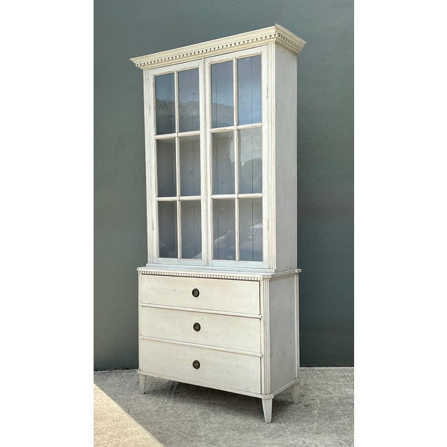 This vintage painted wood and glass cabinet, dating to the mid-20th century, combines practical storage with understated...