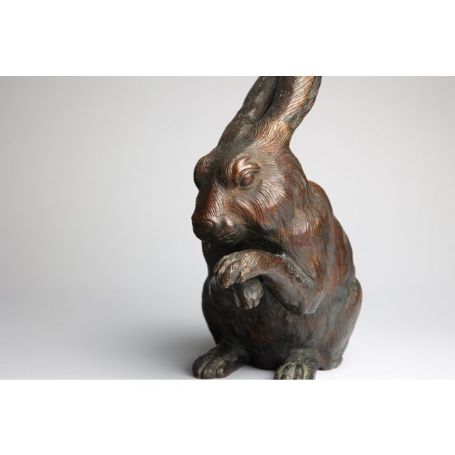 A finely cast Japanese bronze okimono depicting a seated rabbit, its head lowered and both forepaws raised to its face....