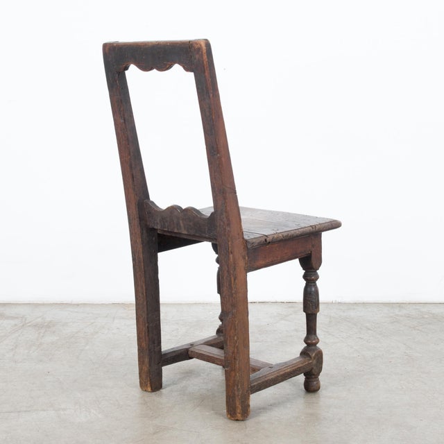 A wooden chair from Belgium, circa 1800. An upright shape with a striking open-framed backrest and a square paneled seat...