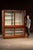 Two-piece oak display cabinet featuring sliding glass doors and adjustable interior shelving. The upper section houses...
