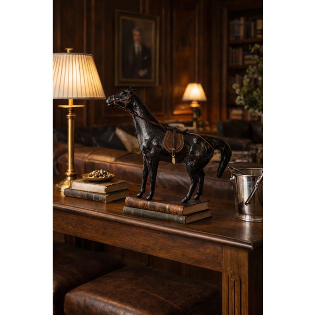 Vintage black horse sculpture detailed with a genuine-looking brown saddle, bridle and equestrian tack. The elongated...