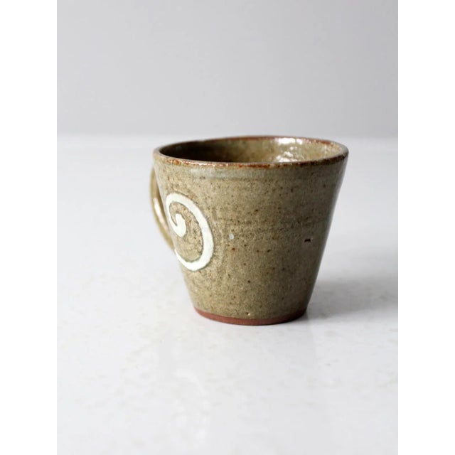 This is a vintage studio pottery mug. Signed by the artist, the hand-crafted mug features an olive green speckled glaze...
