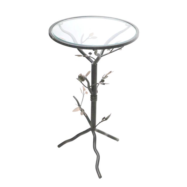 Whimsical decorative occasional side table having a metal foliate base with a bird perched in a branch, and a glass top....