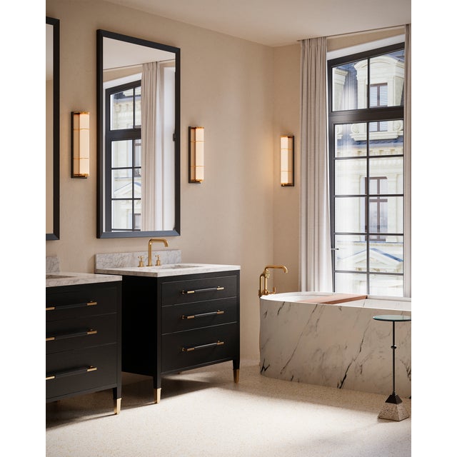 The Blaine Bronze Bath Wall Sconce has a tubular design, with a milky glass tube set into the metal rings in a polished...