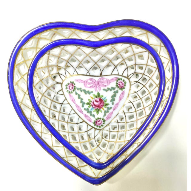 A delicate pair of vintage porcelain heart-shaped trinket dishes featuring open latticework, cobalt blue rims, and hand-...