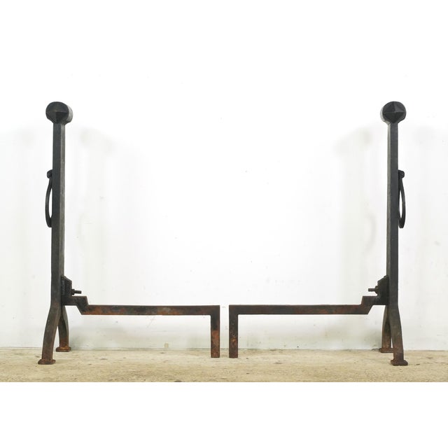 Antique Arts & Crafts style andirons made of cast iron with a loose ring on the front attached to a vertical post....