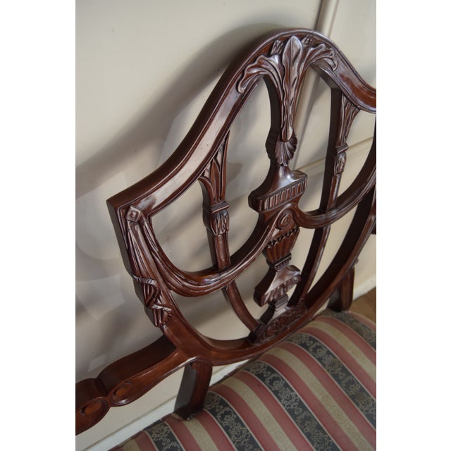 A beautifully carved late 19th- to early 20th-century Hepplewhite-style settee, showcasing the classic shield-back design...