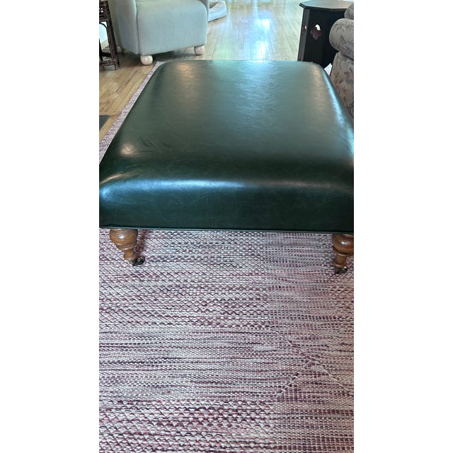 traditional custom made ottoman with medium stained turned lags and brass casters. upholstery is a dark green pleather...