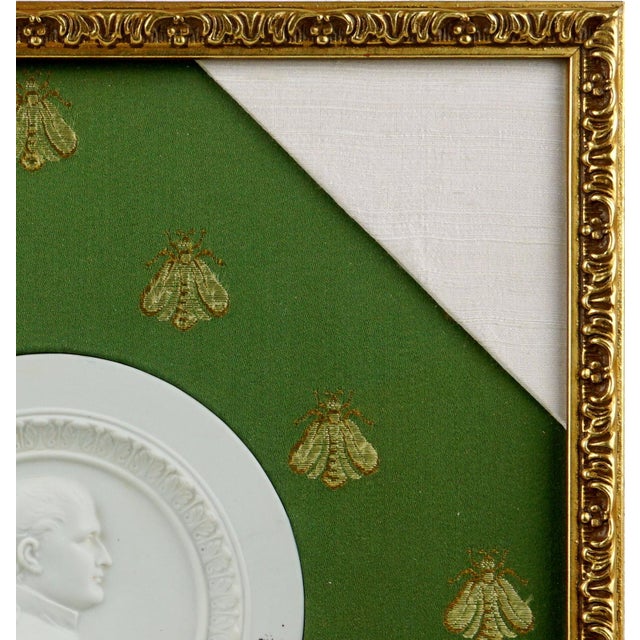 White background with a circular shape, decorated in the center with the profile of Emperor Napoleon I, his head turned to...