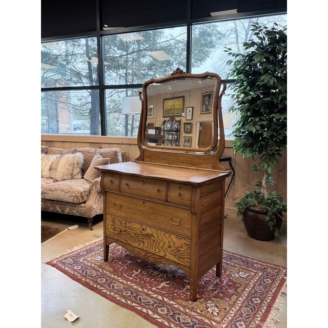 Early 20th century golden oak dresser with a serpentine front and attached shaped mirror. The dresser features two small...