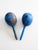 A vintage Mexican wood maracas, hand-painted in a saturated cobalt blue and decorated with whimsical folkloric figures in...