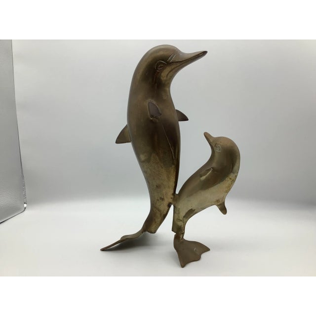A cute mama and baby brass dolphin statue. The baby dolphin is staring at the mama dolphin. The brass dolphins are in...
