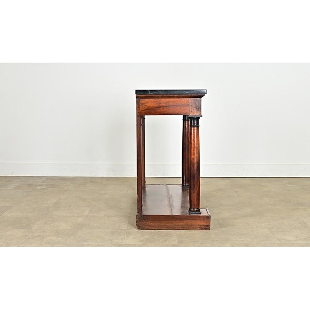 A French 19th century mahogany console in the Empire style with dark stone top. The dense, marbleized stone of charcoal-...