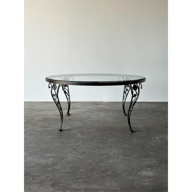 Sculpted blooms and curling vines wind down the four slender legs of this vintage Woodard coffee table, each ending in a...