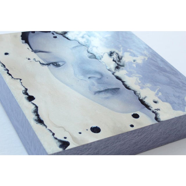 This artwork features a serene, close-up portrait of a contemplative figure, rendered in a cool palette of blues and...