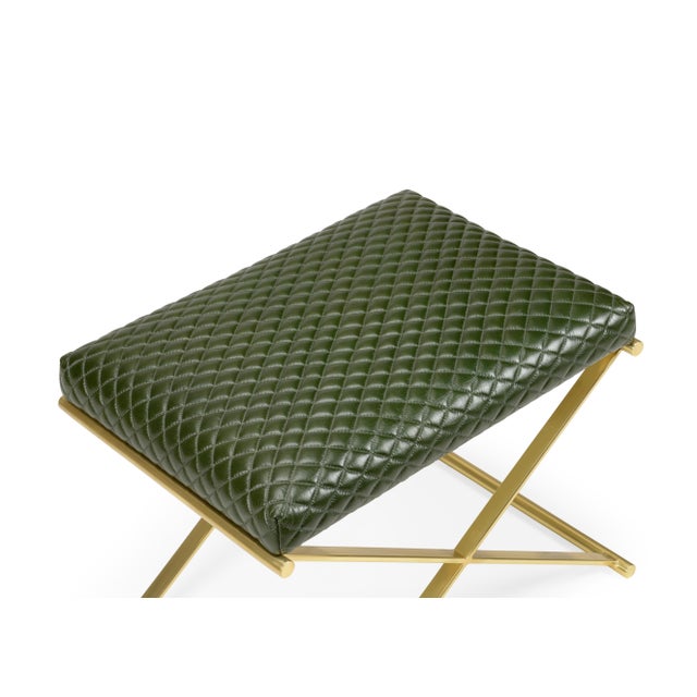 The Garrett Leather Stool has a polished brass "X" base and a green leather seat. The seat has a crisscross pattern...
