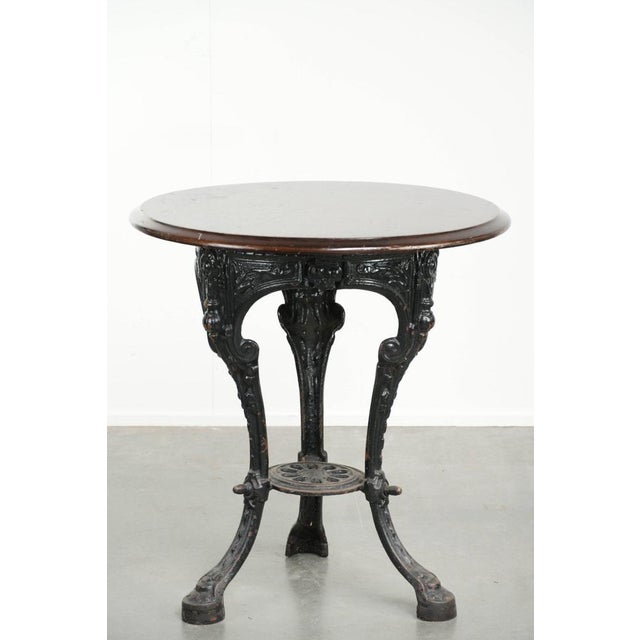 This antique English pub, bistro, or side table from the 19th century combines a round wooden tabletop with a cast-iron...