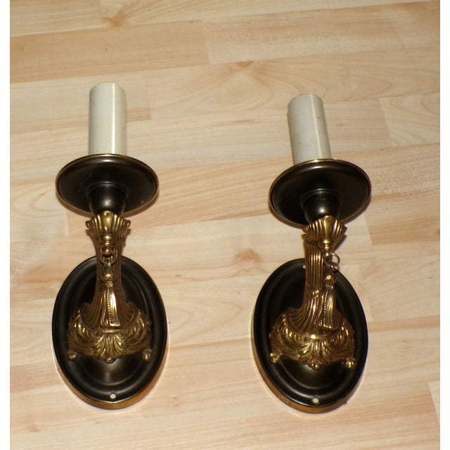 Antique Pair French Style Brass Wall Sconces features sculptural arms attached to oval wall plates with brown finish, and...