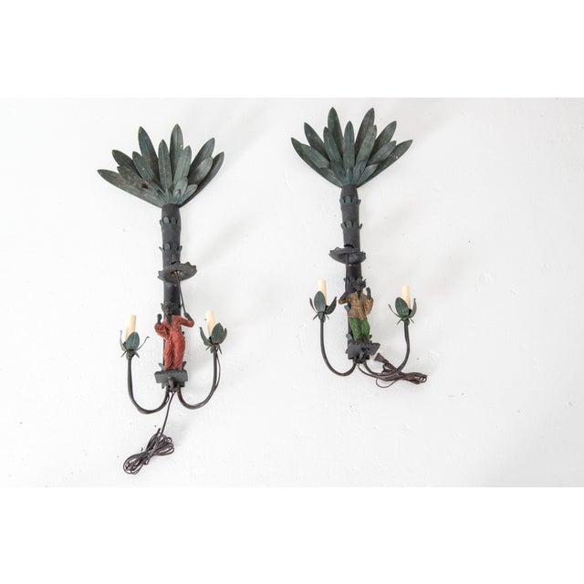 A substantial and unusual pair of Chinoiserie Palm and Figural Sconces. One figure is wearing red clothing. The other...