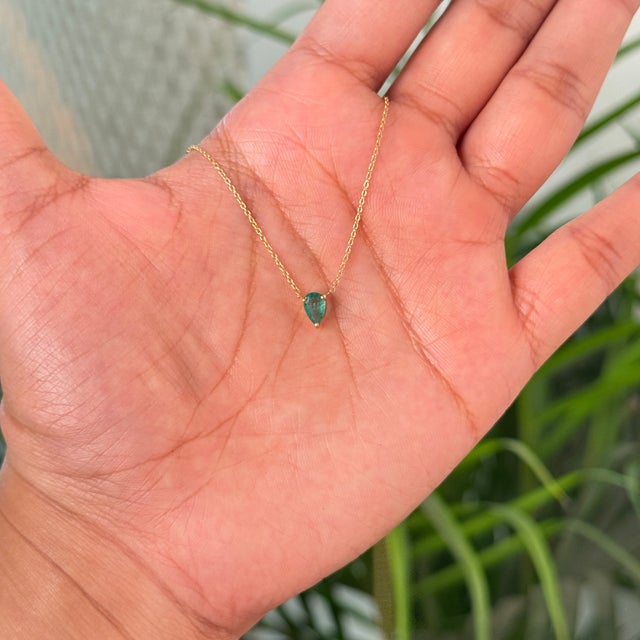This pendant necklace features a 0.36 carat pear-cut natural Zambian emerald set in 18K yellow gold. The emerald measuring...