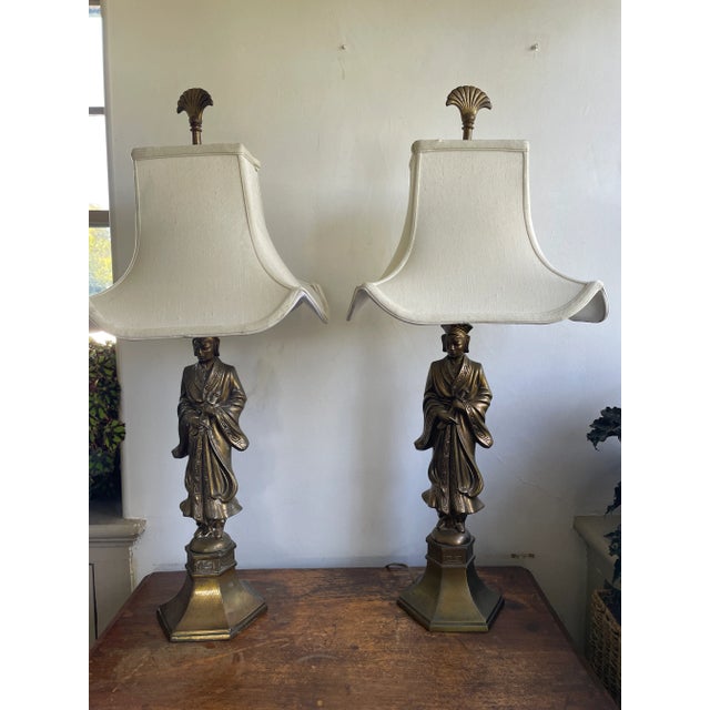 A striking pair of Hollywood Regency figural table lamps featuring robed Asian figures rendered in a rich bronze-tone...