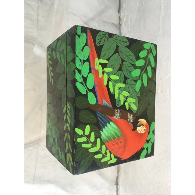 This vintage paper mache box is hand painted. It depicts a parrot and palm leaves. The interior is solid black