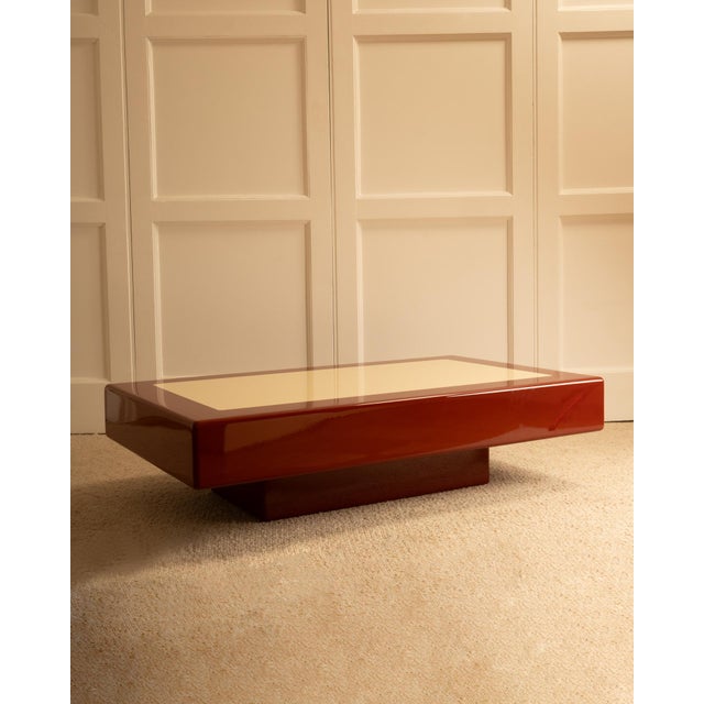 1970s coffee table with a thick rectangular top. Lacquered in vintage brown and red tones with a cream-colored rectangular...