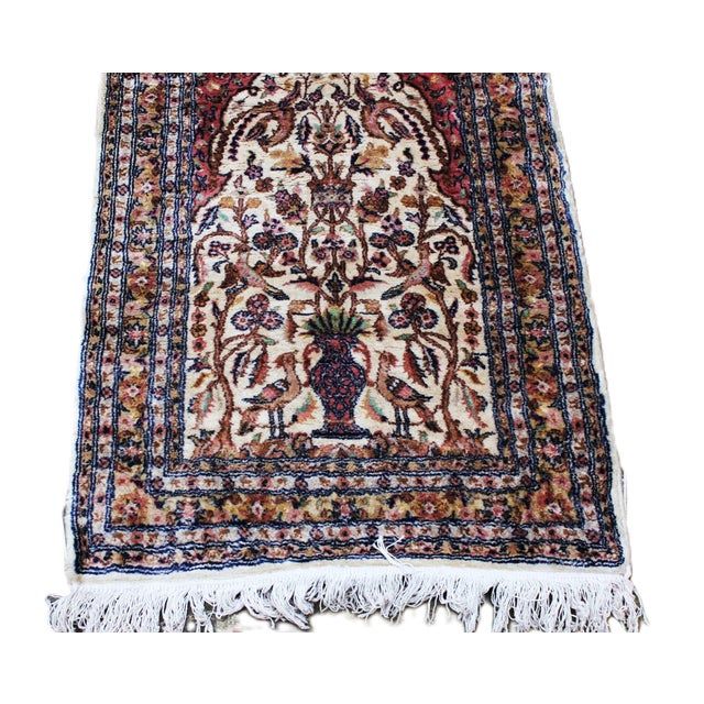 This vintage wool rug features an elegant floral and bird motif arranged around a central vase composition, framed by a...